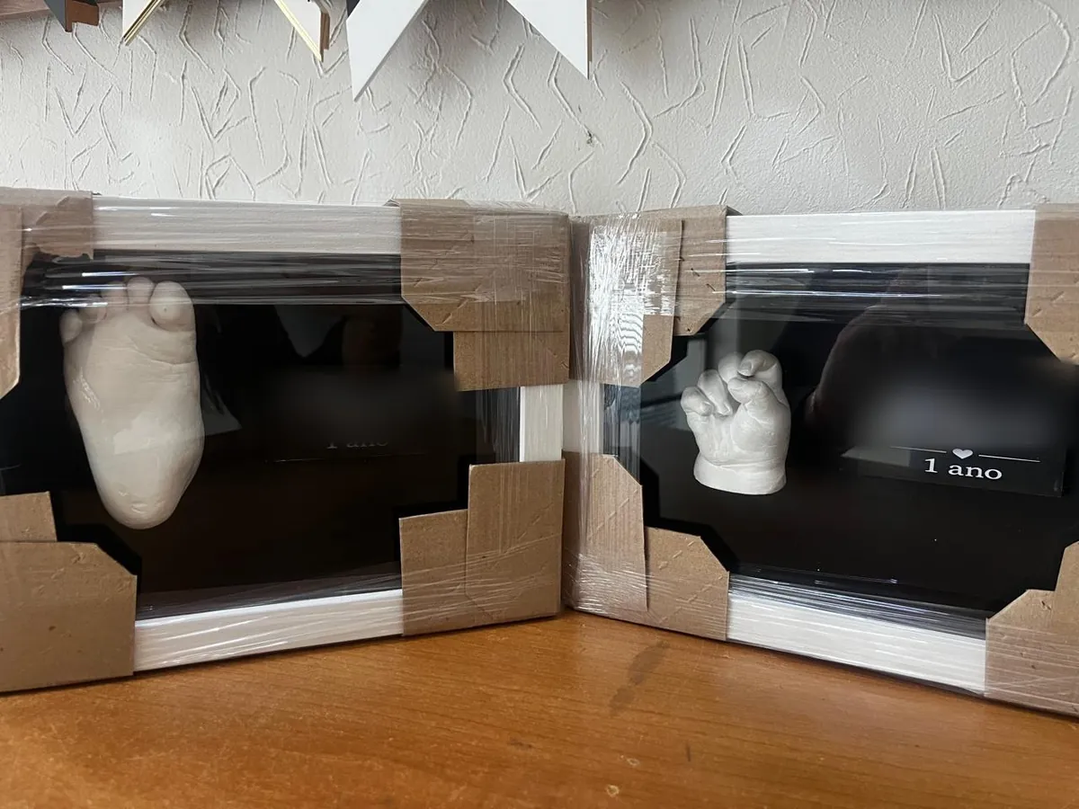 Moldes em gesso do pé e da mão de bebê em quadros caixa com fundo preto e plaquinha de 1 ano