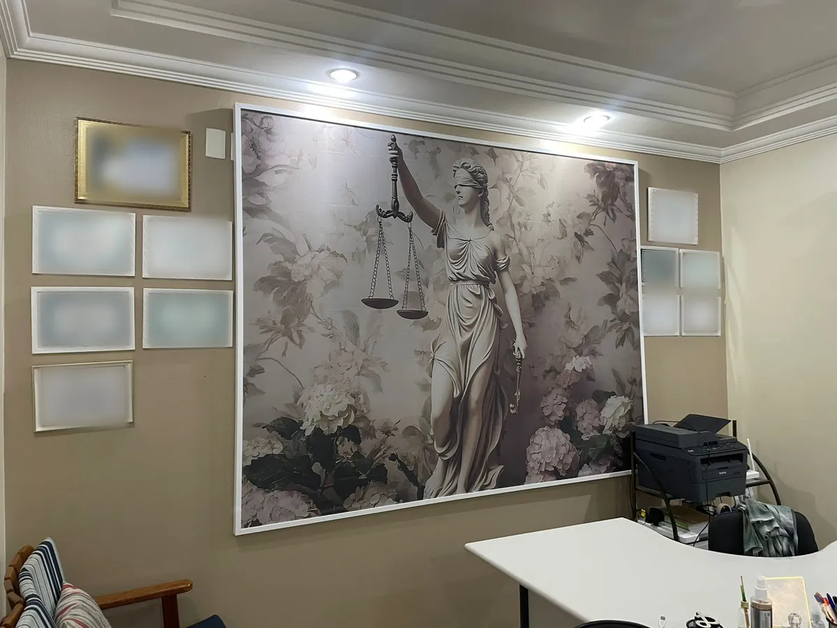 Tela grande com a deusa da Justiça e flores, emoldurada em moldura branca, na parede de um escritório de advocacia